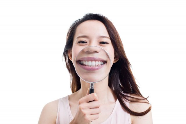 person holding up a magnifying glass and smiling behind it with lingual braces